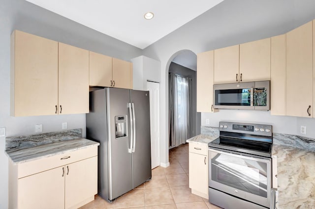 kitchen featuring stainless steel appliances, light tile patterned flooring, cream cabinetry, and light stone countertops