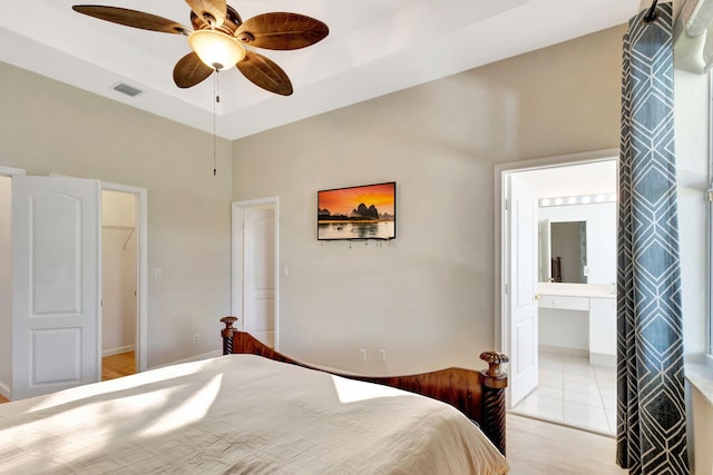 bedroom with a closet, ensuite bath, ceiling fan, a tray ceiling, and a walk in closet