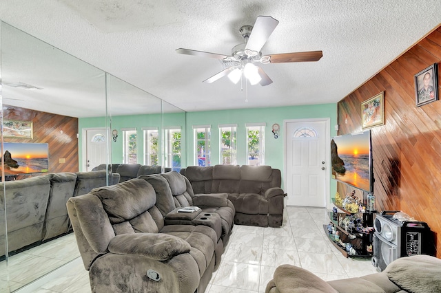 living room with ceiling fan, a textured ceiling, and wooden walls