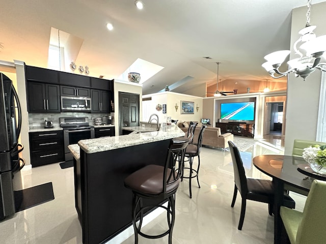 kitchen with tasteful backsplash, stainless steel appliances, lofted ceiling with skylight, a kitchen island with sink, and hanging light fixtures