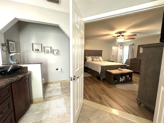 bedroom featuring ceiling fan, sink, light hardwood / wood-style floors, and a textured ceiling