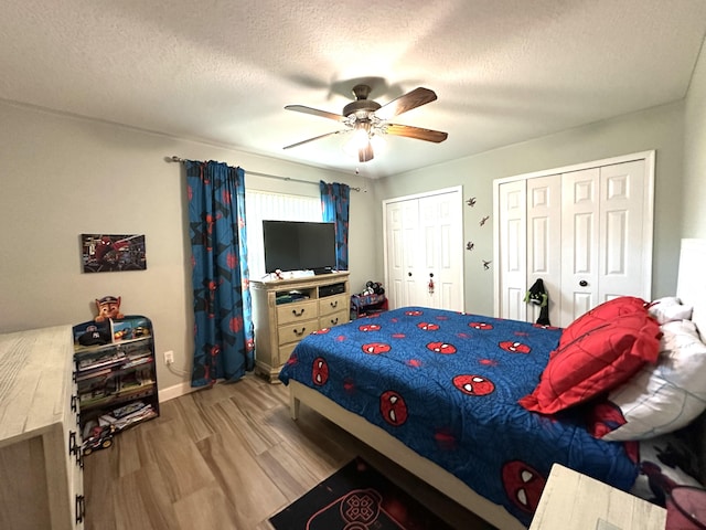 bedroom with a textured ceiling, light wood-type flooring, ceiling fan, and multiple closets