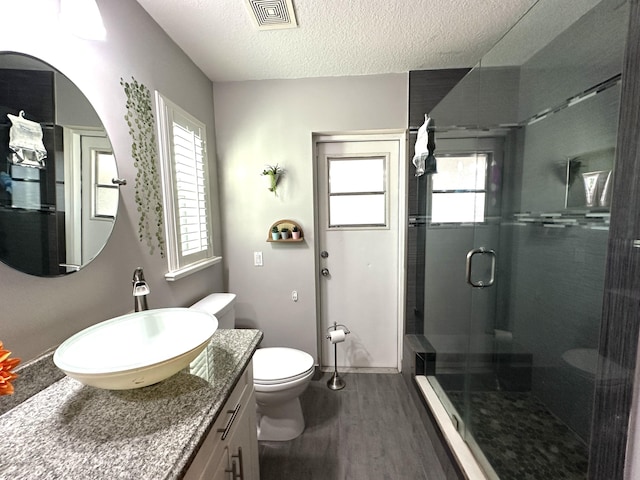 bathroom with a textured ceiling, toilet, wood-type flooring, and walk in shower