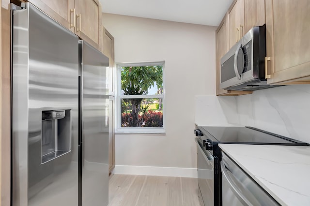 kitchen featuring light brown cabinets, light wood-type flooring, light stone countertops, appliances with stainless steel finishes, and tasteful backsplash