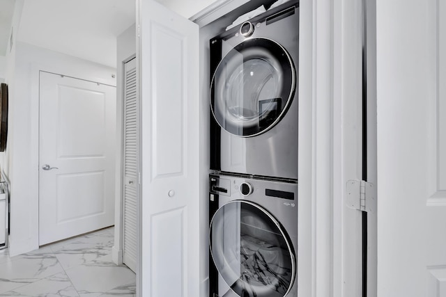 clothes washing area featuring marble finish floor, stacked washer / dryer, and laundry area