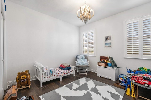 bedroom with a chandelier, dark wood-type flooring, and a nursery area