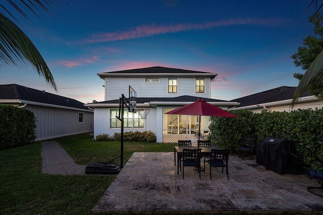 back house at dusk featuring a lawn and a patio area