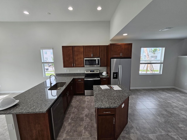 kitchen with sink, dark stone countertops, appliances with stainless steel finishes, a kitchen island, and dark brown cabinetry