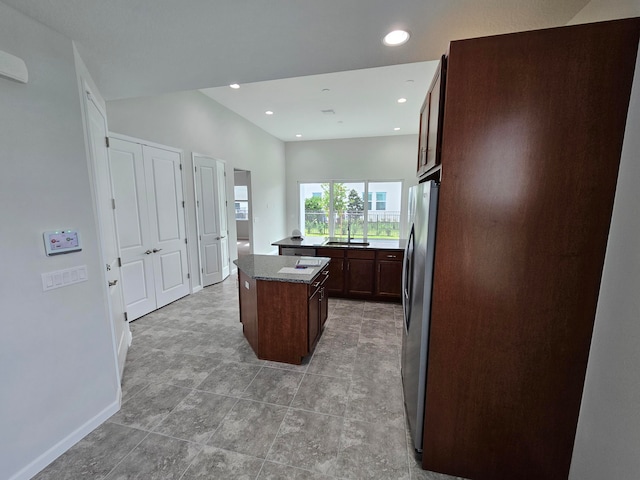 kitchen with dark brown cabinets, a center island, stainless steel refrigerator, and sink