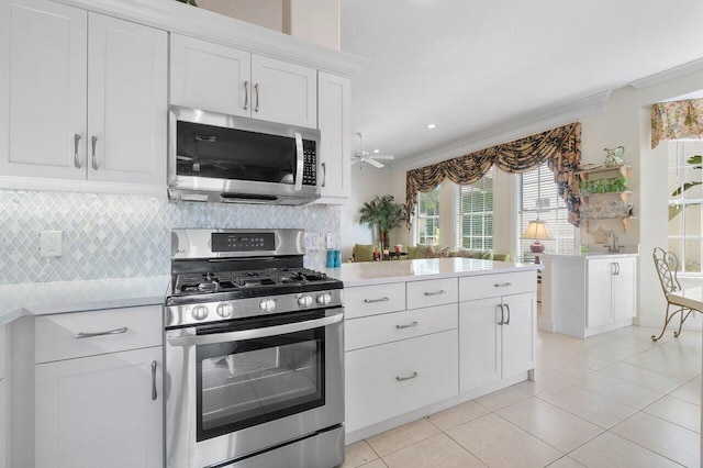 kitchen with light tile patterned floors, tasteful backsplash, appliances with stainless steel finishes, white cabinets, and ornamental molding