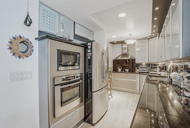 kitchen with pendant lighting, wall chimney range hood, light hardwood / wood-style flooring, decorative backsplash, and appliances with stainless steel finishes