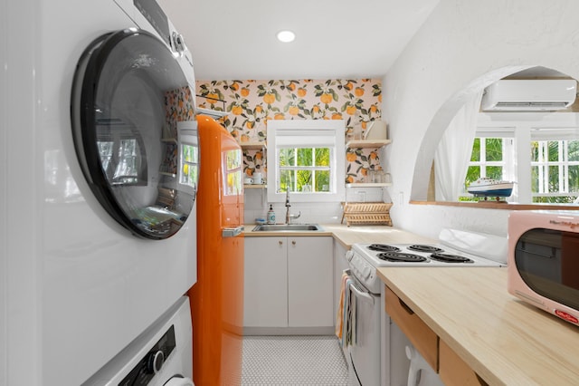 kitchen with white appliances, a wall unit AC, sink, stacked washer and dryer, and plenty of natural light