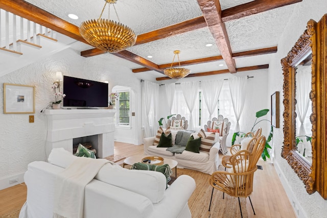 living room with beam ceiling, a tiled fireplace, a textured ceiling, and light wood-type flooring