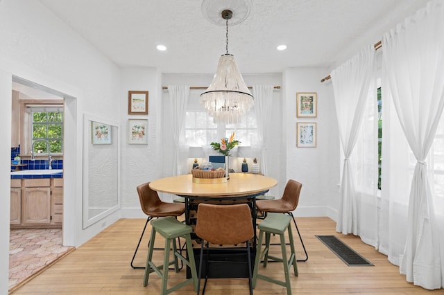 dining area featuring sink, light hardwood / wood-style flooring, a textured ceiling, and a notable chandelier