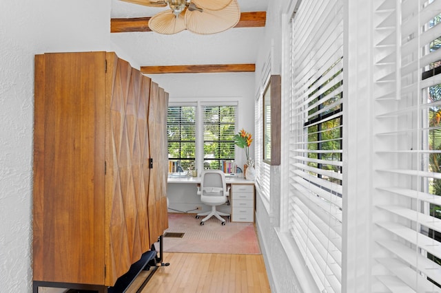 home office with ceiling fan, beam ceiling, built in desk, and light hardwood / wood-style flooring