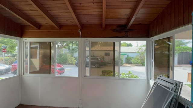 unfurnished sunroom featuring beamed ceiling, a healthy amount of sunlight, and wood ceiling