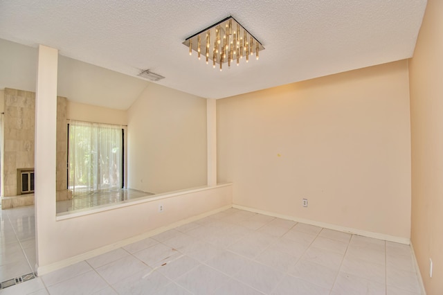 tiled empty room with a large fireplace, a textured ceiling, and vaulted ceiling