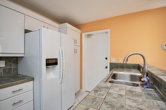 kitchen with light tile patterned floors, white cabinetry, tasteful backsplash, white refrigerator with ice dispenser, and sink