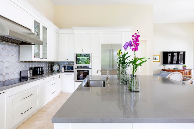 kitchen with wall chimney exhaust hood, stainless steel appliances, sink, a large island with sink, and white cabinetry