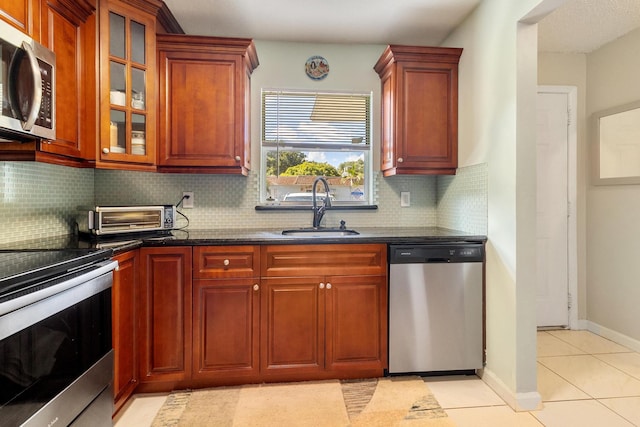 kitchen with backsplash, stainless steel appliances, sink, light tile patterned floors, and dark stone countertops