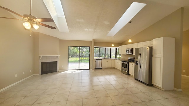 kitchen featuring high vaulted ceiling, a skylight, ceiling fan, appliances with stainless steel finishes, and a tiled fireplace