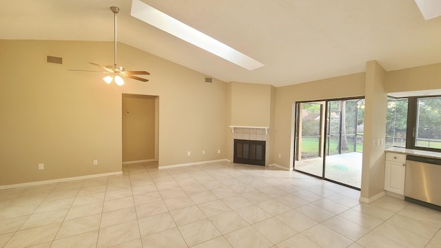 unfurnished living room with a tile fireplace, light tile patterned floors, lofted ceiling with skylight, and ceiling fan