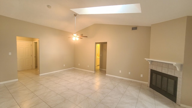 unfurnished living room with a tile fireplace, light tile patterned floors, lofted ceiling with skylight, and ceiling fan