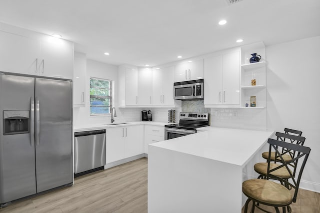 kitchen with white cabinets, sink, light wood-type flooring, kitchen peninsula, and stainless steel appliances