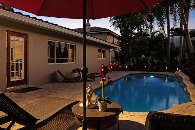 pool at dusk with pool water feature and a patio