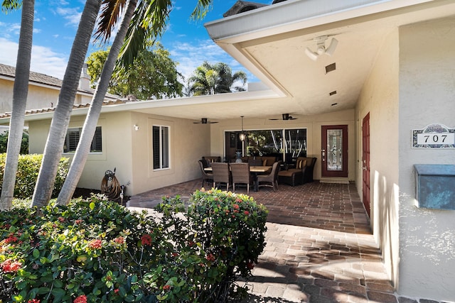 view of exterior entry with a patio area, ceiling fan, and an outdoor living space