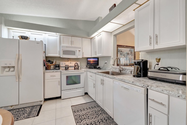 kitchen with white appliances, sink, vaulted ceiling, light tile patterned floors, and white cabinetry