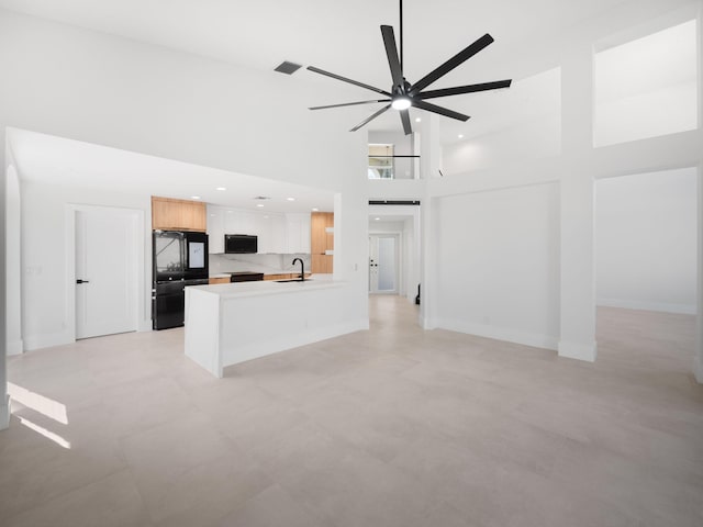 unfurnished living room featuring ceiling fan, sink, and a high ceiling