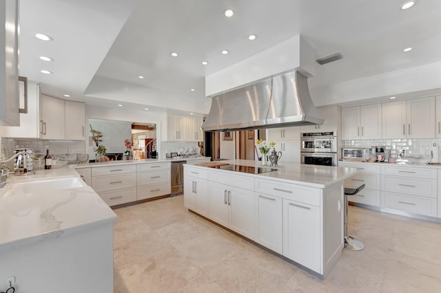 kitchen with decorative backsplash, a large island, island range hood, white cabinetry, and stainless steel appliances