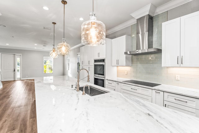 kitchen featuring sink, wall chimney exhaust hood, stainless steel double oven, black electric cooktop, and white cabinets