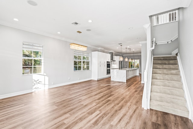 unfurnished living room featuring light wood-type flooring, ornamental molding, and a wealth of natural light