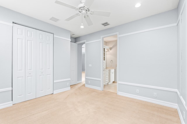 unfurnished bedroom with a closet, light colored carpet, ensuite bath, and ceiling fan