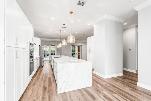 kitchen with sink, a spacious island, decorative light fixtures, white cabinets, and light wood-type flooring