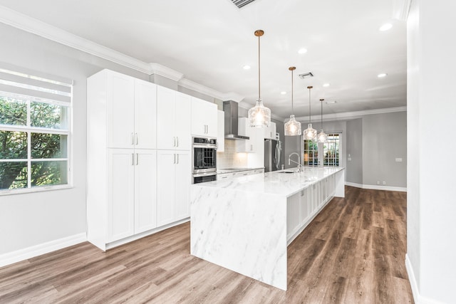 kitchen with pendant lighting, wall chimney range hood, sink, white cabinetry, and stainless steel refrigerator