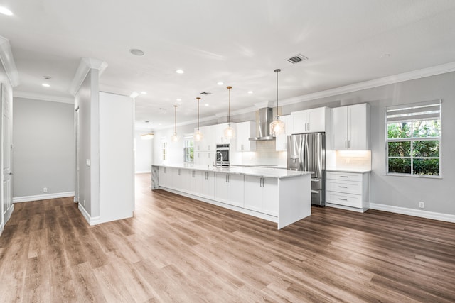 kitchen with white cabinetry, stainless steel appliances, wall chimney range hood, hardwood / wood-style floors, and decorative light fixtures