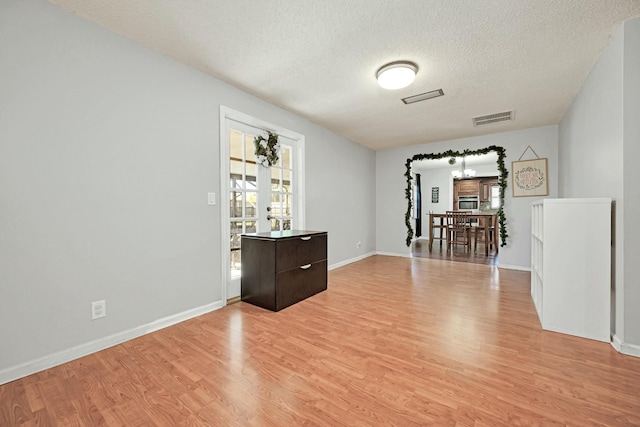 spare room with a textured ceiling, light wood finished floors, visible vents, and baseboards