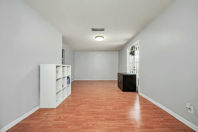 unfurnished living room featuring baseboards, visible vents, light wood-style flooring, and a textured ceiling