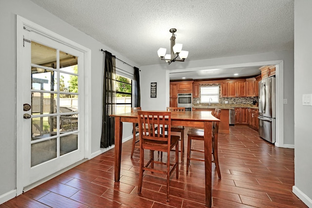 dining area with baseboards, dark wood-style flooring, a textured ceiling, and a notable chandelier