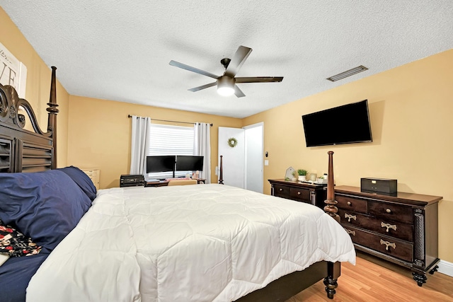 bedroom with a textured ceiling, light wood-style flooring, visible vents, and a ceiling fan