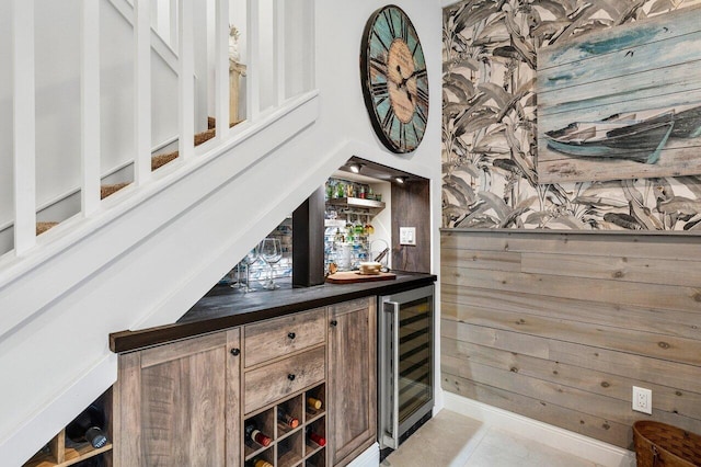 bar featuring wine cooler, light tile patterned flooring, and wood walls