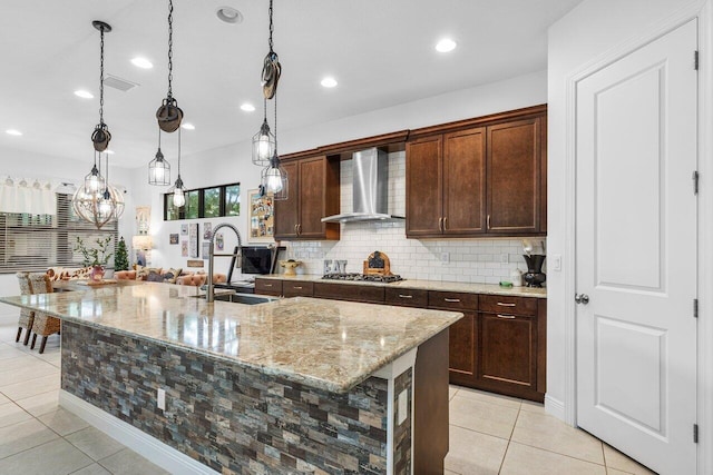 kitchen featuring sink, light stone counters, light tile patterned floors, a kitchen island with sink, and wall chimney range hood