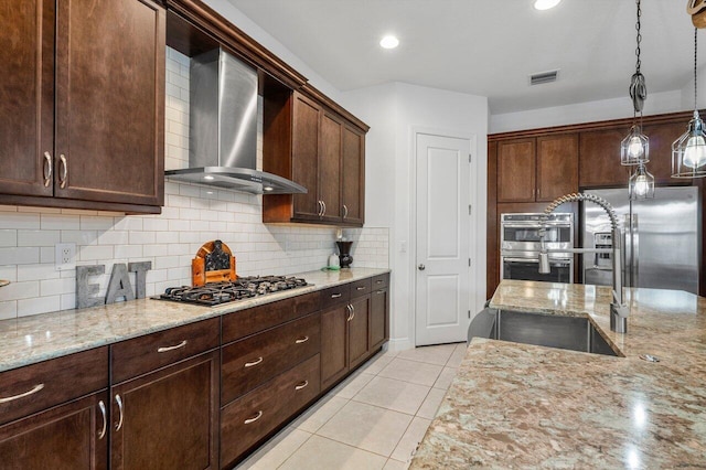 kitchen with pendant lighting, light stone countertops, wall chimney exhaust hood, and appliances with stainless steel finishes