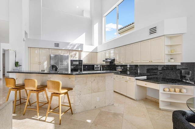 kitchen featuring a high ceiling, tasteful backsplash, cream cabinets, a breakfast bar, and black appliances