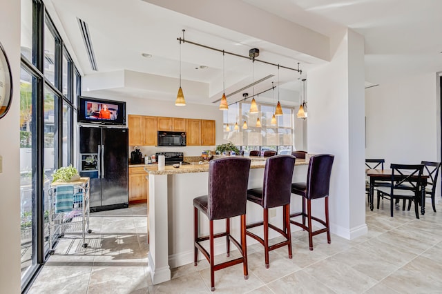 kitchen featuring light stone countertops, hanging light fixtures, black appliances, and a kitchen breakfast bar