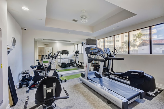 exercise room featuring ceiling fan and a tray ceiling