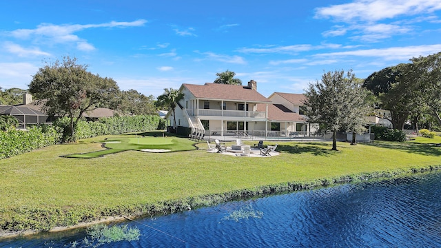 rear view of property featuring a patio, a balcony, a lawn, and a water view